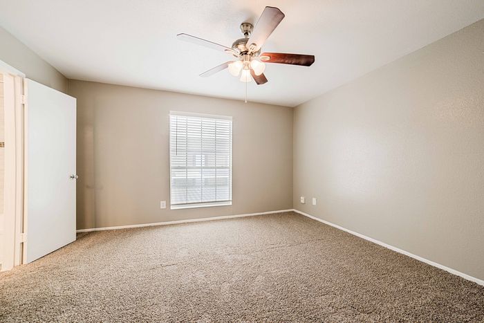 Bright and airy bedroom with plush carpet, neutral walls, and a stylish ceiling fan, perfect for a peaceful retreat.