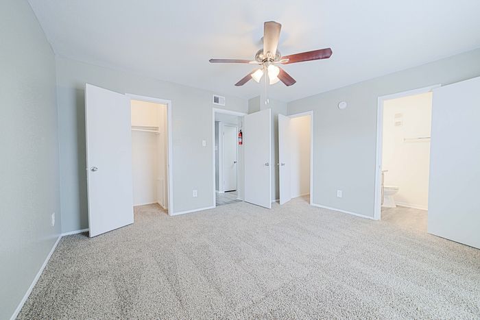Bright and spacious bedroom with plush carpet, ceiling fan, and multiple doors leading to closets and a bathroom.