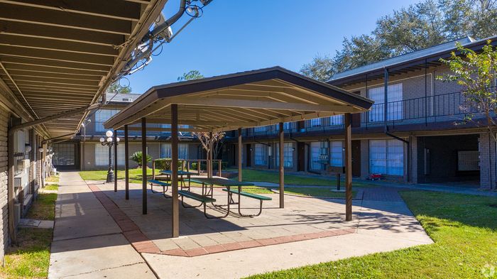 Charming apartment complex with a sunny courtyard featuring a picnic area and well-manicured greenery.