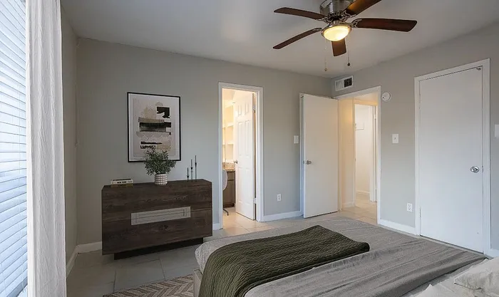 Elegant bedroom featuring a cozy bed, modern dresser, stylish artwork, and ceiling fan for optimal comfort.