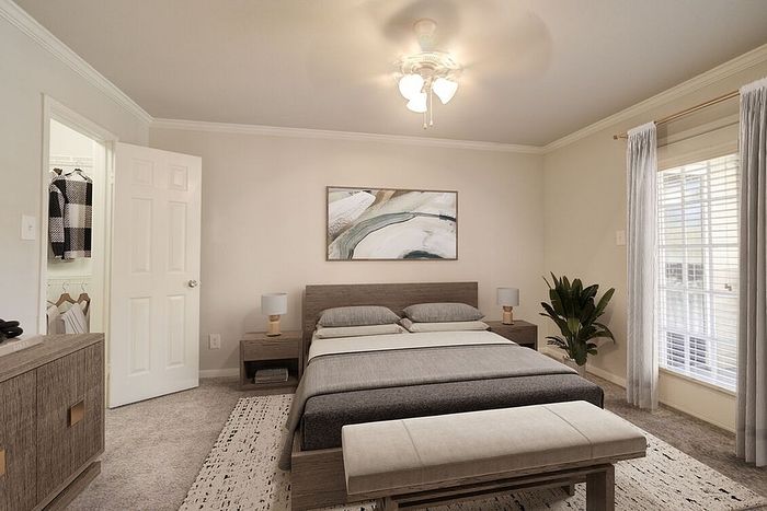 Elegant bedroom featuring a modern gray bed, stylish decor, and a cozy rug, with a walk-in closet and natural light streaming through large windows.
