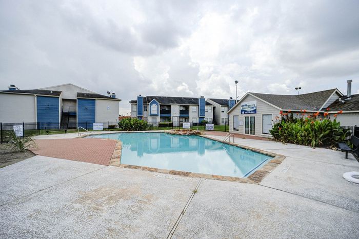 Inviting apartment complex with a sparkling blue pool, surrounded by well-maintained buildings and lush greenery, perfect for relaxation.