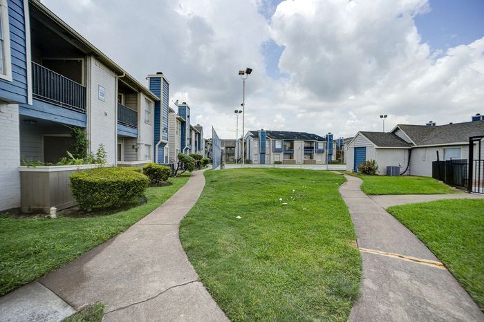 Charming apartment complex with vibrant blue accents, lush green lawns, and inviting walkways under a bright sky.