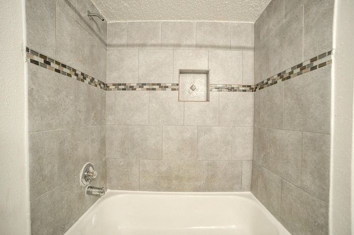 Modern bathroom featuring elegant gray tiles, a sleek built-in shelf, and contemporary mosaic accents.