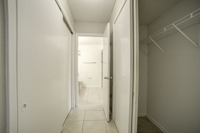 Inviting hallway featuring a spacious closet, elegant tiled floor, and a glimpse into a bright bathroom, offering ample storage and modern design.