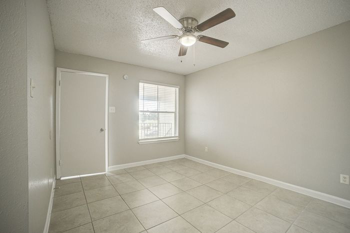 Bright and modern empty room with sleek tile flooring, neutral gray walls, and a stylish ceiling fan. Perfect canvas for a cozy living space.