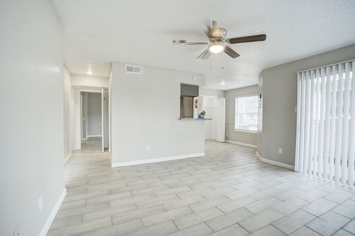 Contemporary open-plan living space featuring elegant tile flooring, ceiling fan, and bright windows.