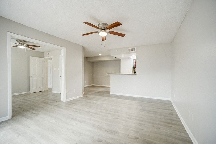 Inviting living space with modern light wood flooring, ceiling fan, and an open layout leading to a cozy kitchen area.