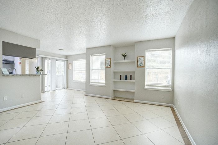 Bright and airy living room with sleek tile flooring, modern open kitchen, and large windows providing ample natural light.