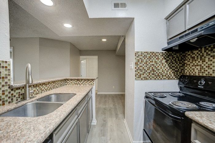 Modern apartment kitchen with sleek countertops, mosaic backsplash, and elegant stainless steel sink.