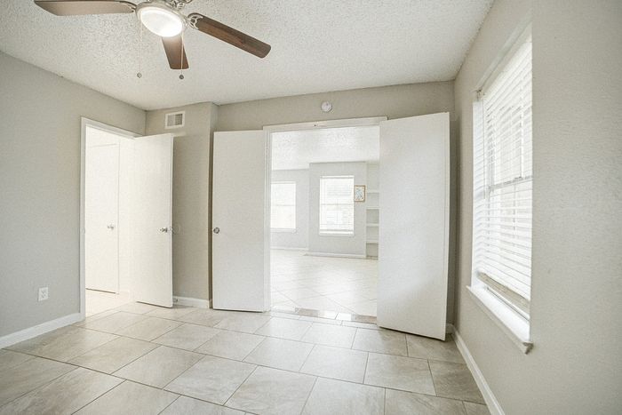 Bright and inviting room with elegant floor tiles, modern ceiling fan, and ample natural light through large windows.