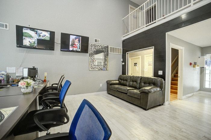 Modern communal lounge featuring a comfortable leather sofa, chic workspace with blue chairs, and flat-screen televisions on a stylish grey wall.