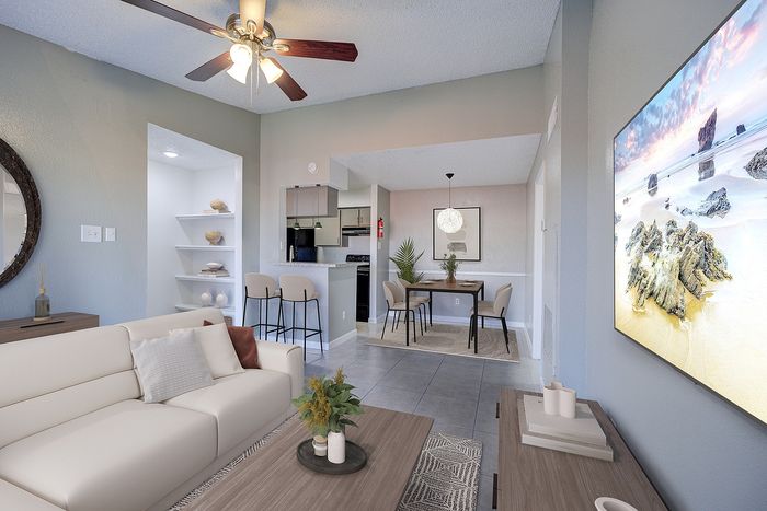 Modern apartment living room with a cozy white sofa, open-concept dining area, stylish kitchen bar, and serene beach art on the wall.