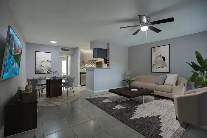 Modern open-concept living room and dining area with elegant decor, featuring a cozy sofa, stylish dining set, and contemporary artwork. The space is illuminated by a ceiling fan, while sleek kitchen appliances peek through chic cabinetry.