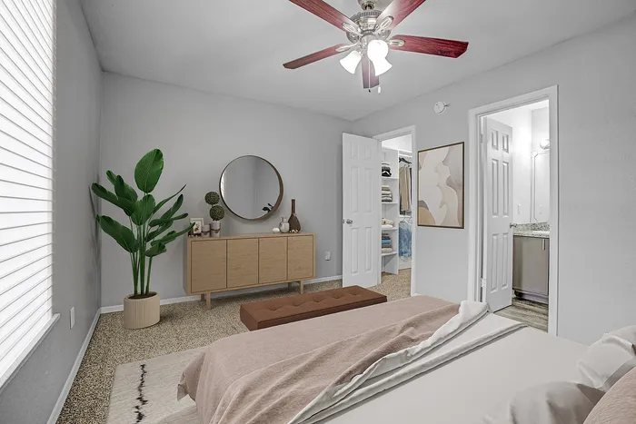 Chic bedroom with modern decor, featuring a plush bed, stylish dresser, vibrant plant, and convenient walk-in closet access.