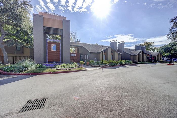 Inviting apartment complex entrance with modern architecture and lush landscaping under a bright blue sky.