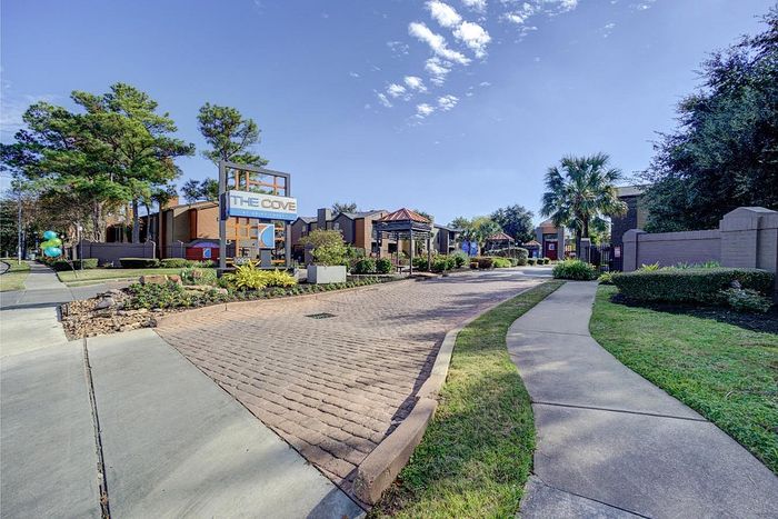 Charming entrance to The Cove apartments featuring lush greenery, cobblestone pathways, and modern architectural design.