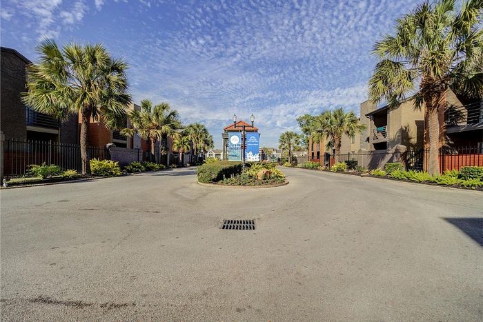 Inviting apartment complex entrance with lush palm trees and well-maintained landscaping under a bright, blue sky.