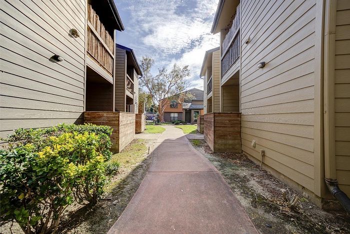 Charming walkway bordered by lush greenery leading to cozy townhouses under a serene blue sky.