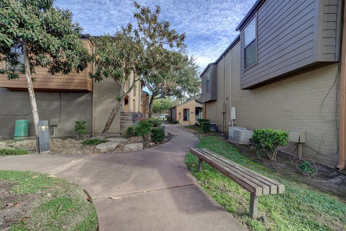 Charming townhouse exterior with landscaped pathways, mature trees, and cozy outdoor seating.