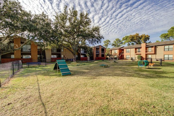 Charming apartment complex with a lush, pet-friendly park featuring agility equipment and shaded by mature trees.
