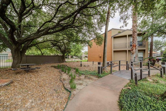 Charming apartment exterior nestled among lush trees, featuring a serene pathway and a cozy picnic area for relaxation.