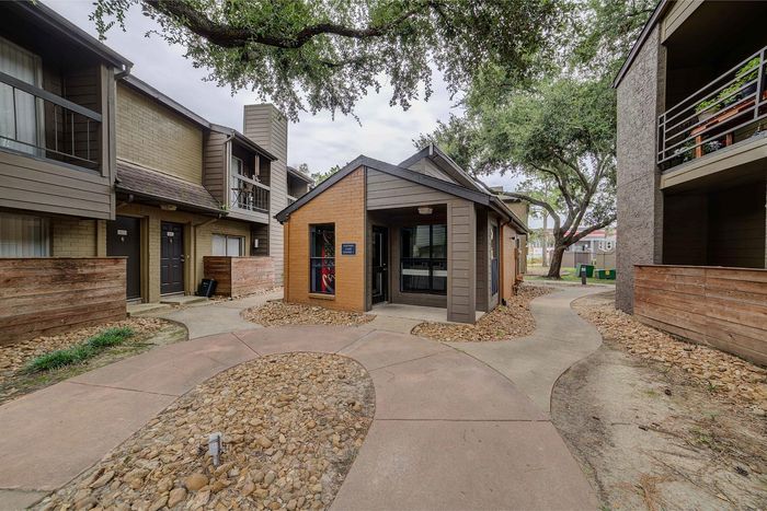 Inviting apartment complex with charming brick and wood accents, surrounded by lush greenery and winding pathways.