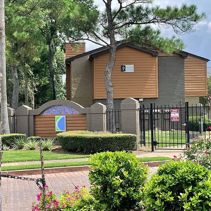 Charming apartment community entrance surrounded by lush greenery and featuring contemporary architecture.