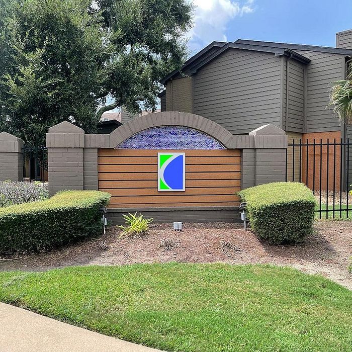 Charming apartment entrance with modern signage surrounded by lush greenery and well-maintained landscaping.