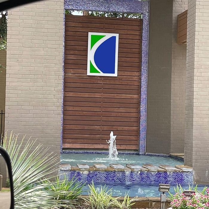 Elegant apartment entrance featuring a modern water fountain with vibrant landscaping and stylish wooden paneling.