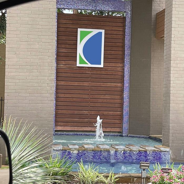 Elegant entrance with a modern water feature, stylish logo, and lush greenery, offering a welcoming and serene ambiance.