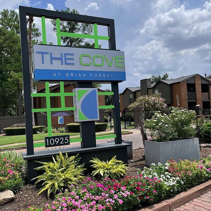 Elegant entrance sign of The Cove at Briar Forest surrounded by vibrant landscaping, offering a glimpse of the inviting apartment community.