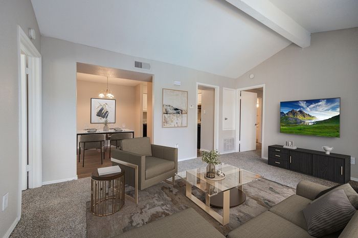 Modern living room with elegant decor, featuring cozy sofas, a glass coffee table, and a mounted TV, leading to a stylish dining area in a well-lit, open-concept space.