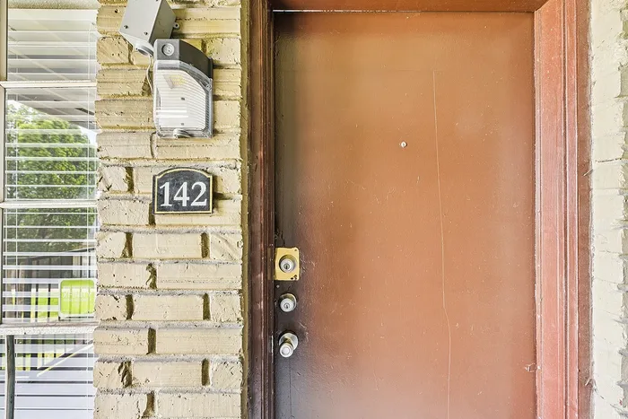 Inviting entrance with a sturdy wooden door and stylish brick exterior, featuring a welcoming light fixture and modern numbered sign.
