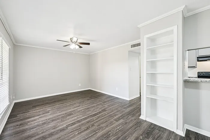 Elegant living room with dark wood flooring, built-in shelves, modern ceiling fan, and ample natural light from large windows.
