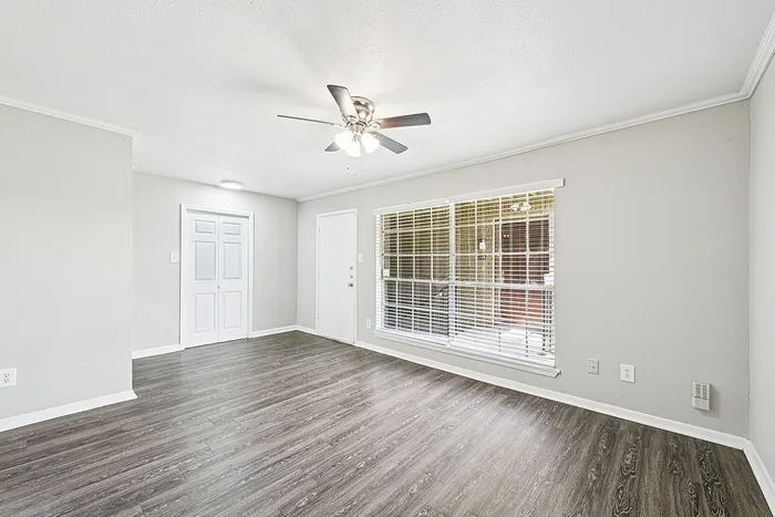 Bright and airy living room featuring sleek hardwood floors, a modern ceiling fan, and large windows with white blinds.