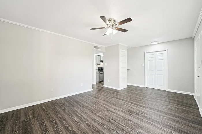 Bright and airy living space featuring elegant wood flooring, modern ceiling fan, and a seamless transition to the kitchen with crafted built-in shelving.
