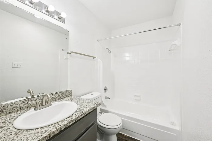 Bright and modern bathroom featuring granite countertops, sleek fixtures, and a pristine bathtub with tiled wall design.