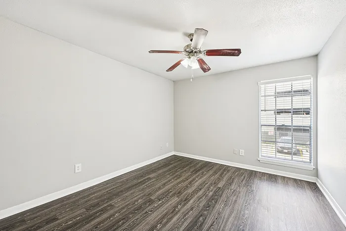 Bright, spacious room with modern wood flooring, large window, and elegant ceiling fan, perfect for personalization.