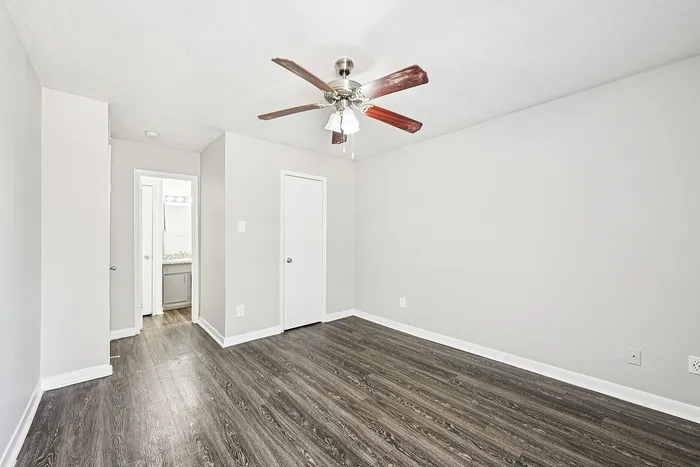 Bright and spacious bedroom with elegant wood flooring, modern ceiling fan, and ample natural light.