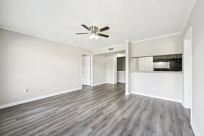 Elegant open living space with modern wood flooring and a stylish ceiling fan, adjacent to a spacious kitchen with a breakfast bar.