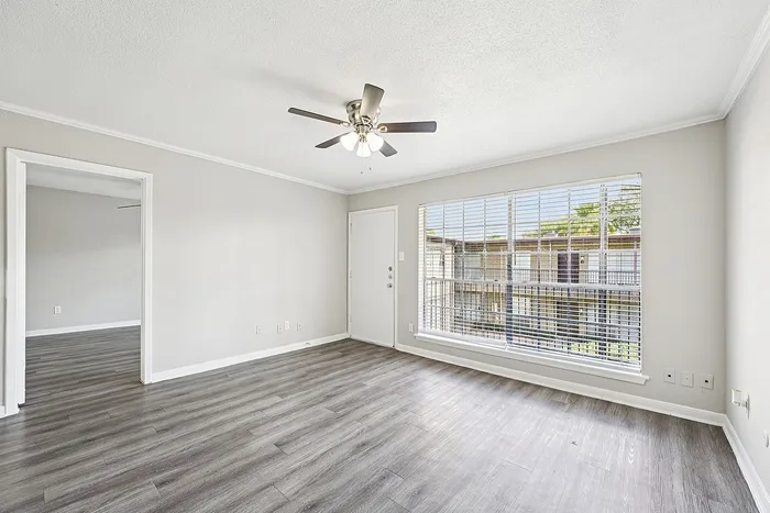 Bright and airy living room with sleek vinyl flooring, large windows, and a ceiling fan offering ample natural light and modern comfort.