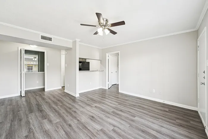 Bright and spacious living area with modern wood flooring and ceiling fan, leading to a sleek open kitchen.