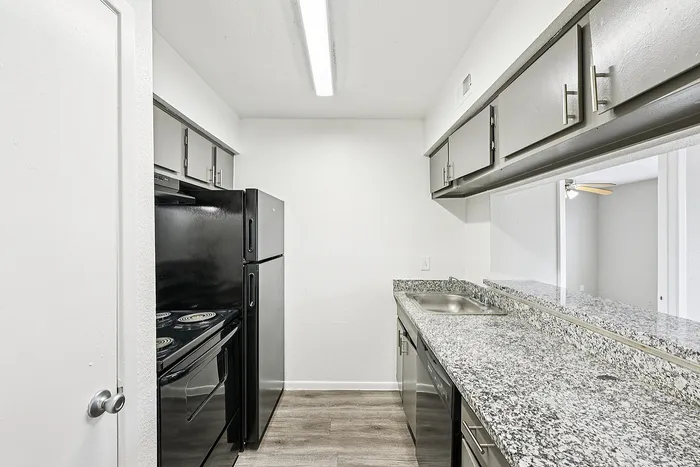 Modern kitchen with sleek black appliances, granite countertops, and stylish wood flooring.