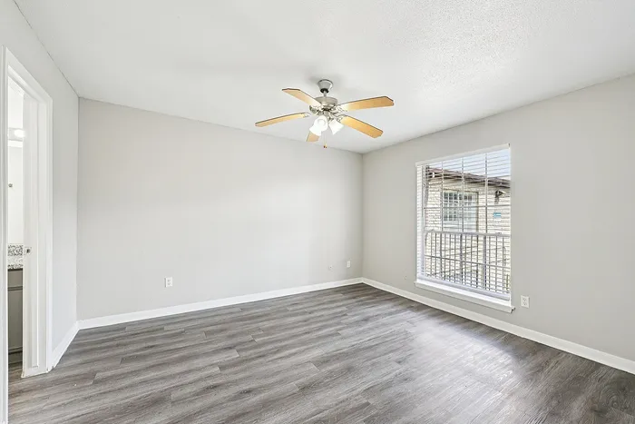Bright and airy room with modern wood flooring, large window, and ceiling fan, ideal for comfortable living.