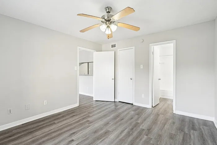 Bright and airy bedroom with elegant wood-look flooring, white walls, and a modern ceiling fan, offering a clean and inviting space.