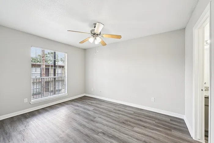 Bright and airy bedroom with stylish wooden flooring, ceiling fan, and large window bringing in natural light.
