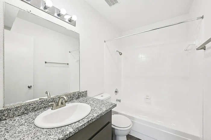 Bright and modern bathroom with elegant granite countertop, spacious mirror, and pristine white fixtures.