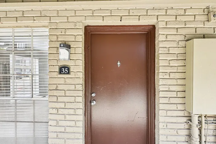 Inviting entrance of a brick-walled apartment with a classic brown door, adorned with a charming welcome light.