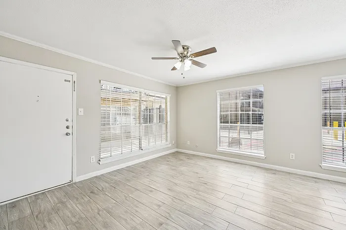 Bright and inviting empty room with modern laminate flooring and large sunlit windows, perfect for creating a cozy living space.